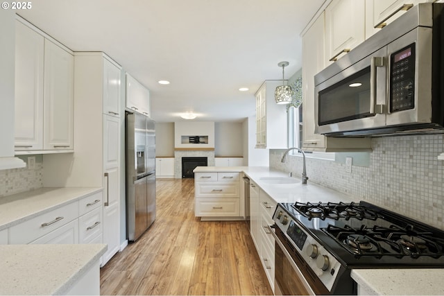 kitchen featuring light wood-style flooring, a sink, open floor plan, white cabinetry, and stainless steel appliances