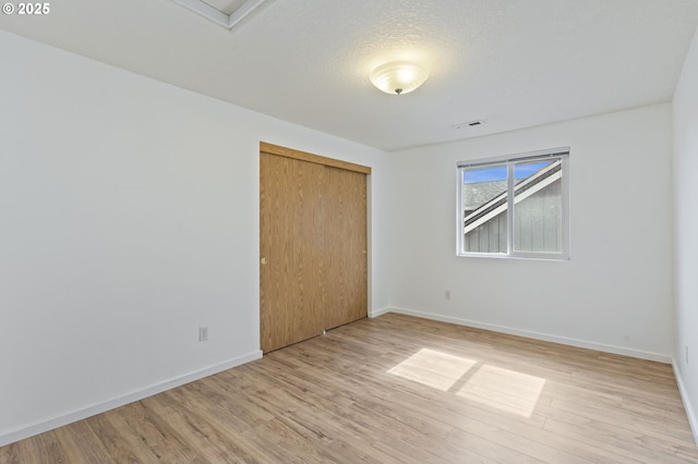 unfurnished room featuring a textured ceiling, light wood-style floors, visible vents, and baseboards