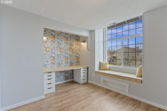 unfurnished office featuring light wood-type flooring, baseboards, a textured ceiling, and visible vents