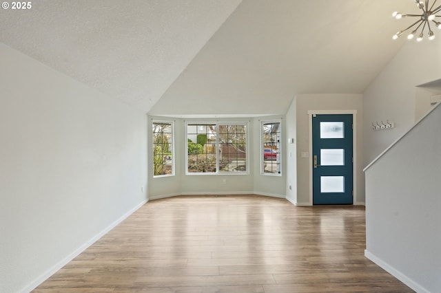 entryway with a notable chandelier, wood finished floors, baseboards, and vaulted ceiling