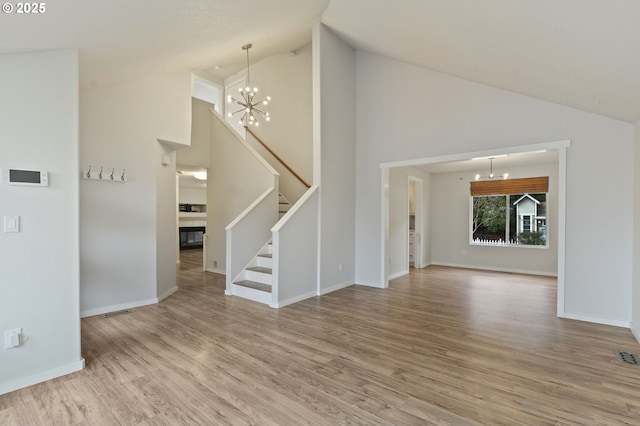 unfurnished living room with wood finished floors, baseboards, stairs, a glass covered fireplace, and a notable chandelier