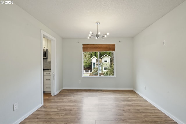 unfurnished dining area with an inviting chandelier, light wood-style flooring, baseboards, and a textured ceiling