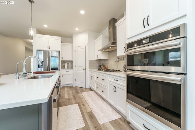 kitchen with stainless steel appliances, sink, wall chimney range hood, and white cabinets