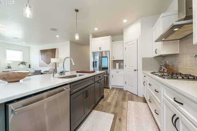 kitchen with pendant lighting, white cabinetry, sink, stainless steel appliances, and wall chimney exhaust hood