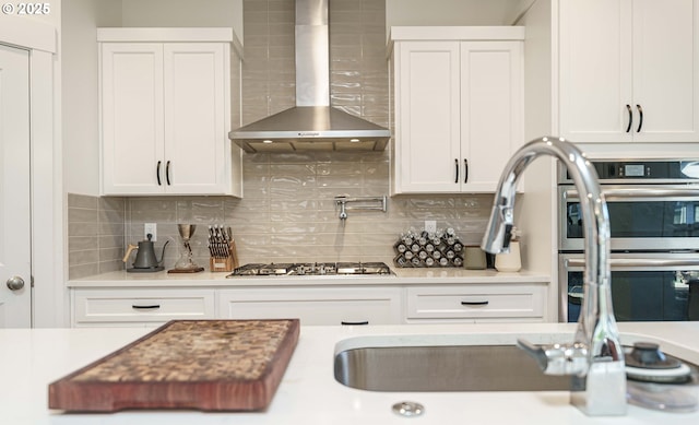 kitchen with tasteful backsplash, appliances with stainless steel finishes, wall chimney exhaust hood, and white cabinets