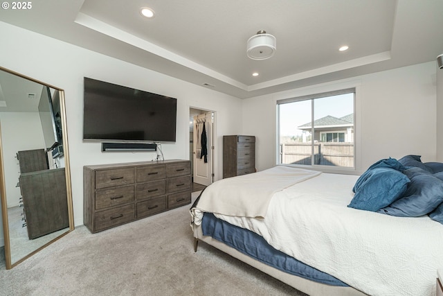 bedroom with light carpet, a tray ceiling, and a walk in closet