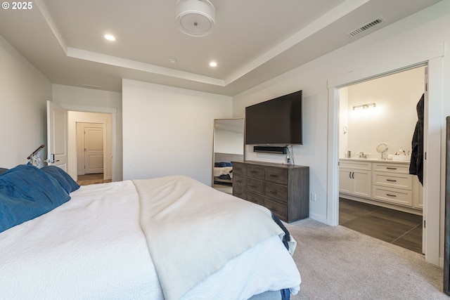 carpeted bedroom with ensuite bath and a raised ceiling