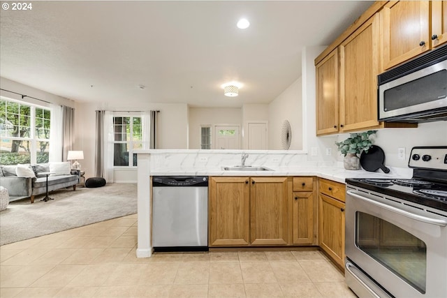 kitchen featuring open floor plan, a peninsula, stainless steel appliances, light countertops, and a sink