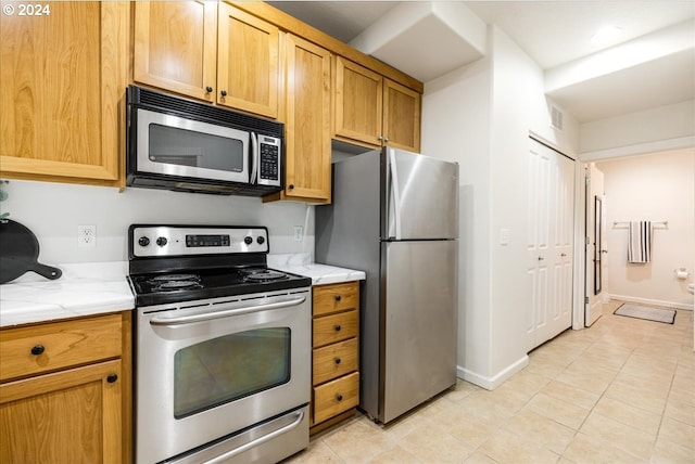 kitchen with light tile patterned floors, baseboards, visible vents, light stone countertops, and stainless steel appliances