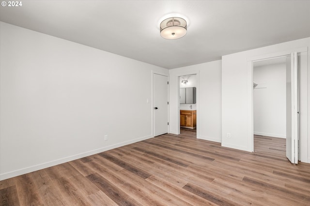 unfurnished bedroom featuring hardwood / wood-style flooring, a walk in closet, ensuite bath, and a closet