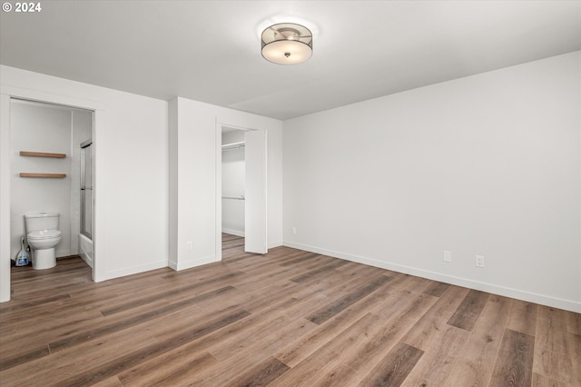 unfurnished bedroom with a walk in closet, hardwood / wood-style floors, connected bathroom, and a closet