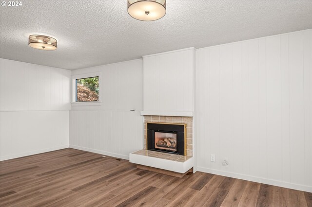 unfurnished living room with wood-type flooring, a tiled fireplace, and a textured ceiling