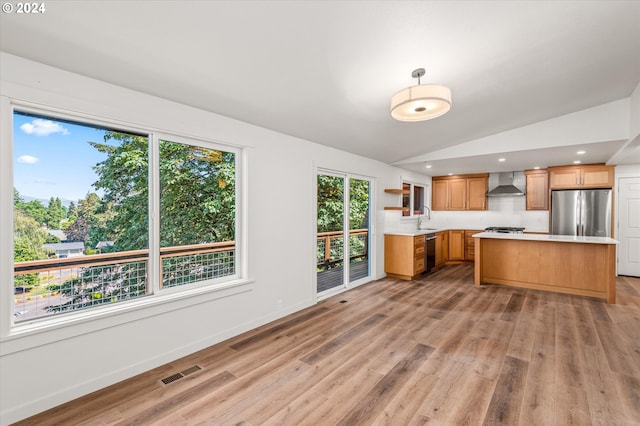 kitchen with sink, stainless steel appliances, vaulted ceiling, wall chimney exhaust hood, and light wood-type flooring