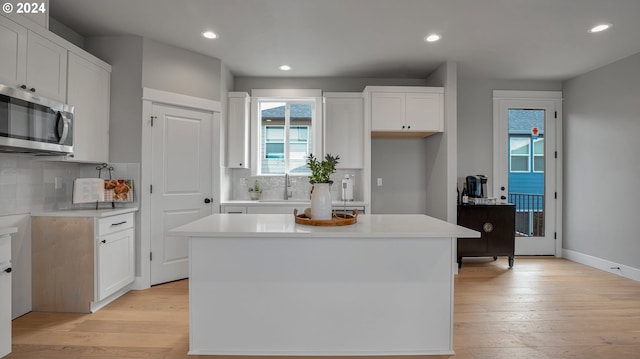 kitchen with decorative backsplash, light wood-style flooring, and stainless steel microwave