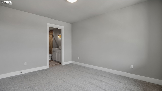 unfurnished bedroom featuring ensuite bathroom, baseboards, and light colored carpet