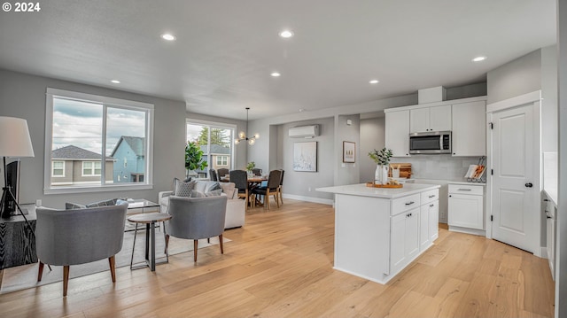 kitchen featuring white cabinets, light wood-style flooring, an AC wall unit, stainless steel microwave, and backsplash