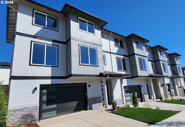 view of front of property featuring stone siding, driveway, an attached garage, and a residential view