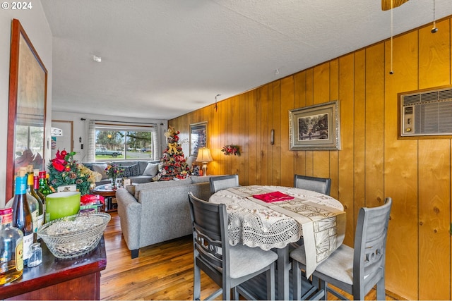 dining space featuring light hardwood / wood-style floors, an AC wall unit, a textured ceiling, and wood walls