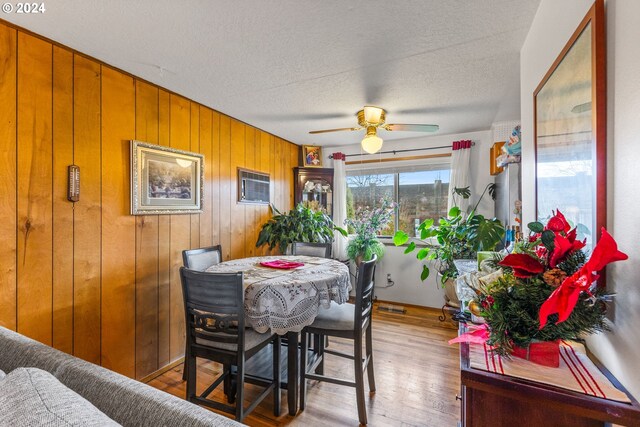 dining area with wood walls, a textured ceiling, an AC wall unit, ceiling fan, and hardwood / wood-style floors