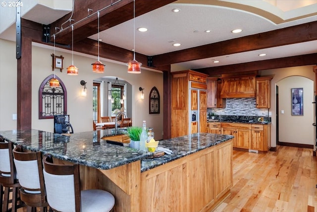 kitchen with hanging light fixtures, light wood-type flooring, dark stone counters, and premium range hood