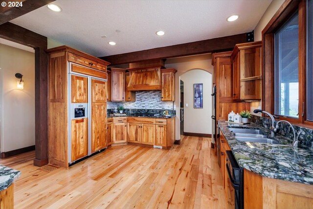 kitchen featuring premium range hood, sink, dark stone countertops, decorative backsplash, and black appliances