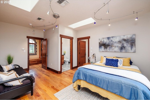 bedroom with light hardwood / wood-style flooring, ensuite bath, a skylight, and track lighting