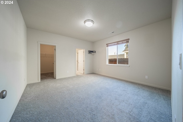 unfurnished bedroom featuring a walk in closet, a textured ceiling, a closet, and carpet flooring