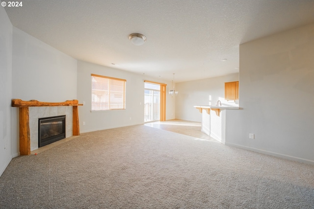 unfurnished living room with a textured ceiling, light carpet, a fireplace, and a chandelier