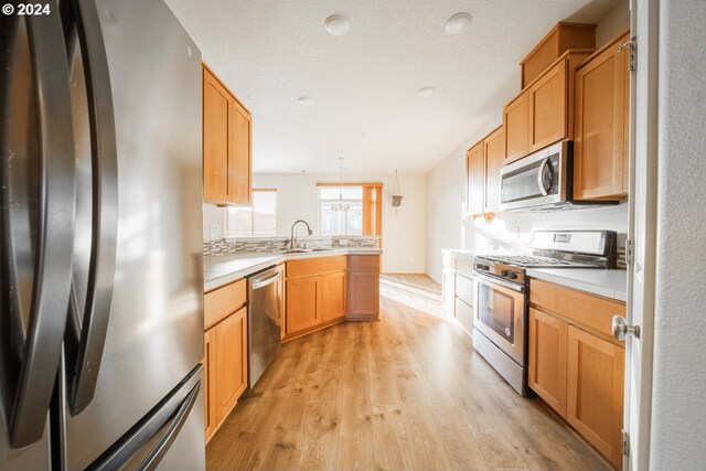 kitchen featuring stainless steel appliances, sink, pendant lighting, light wood-type flooring, and a textured ceiling