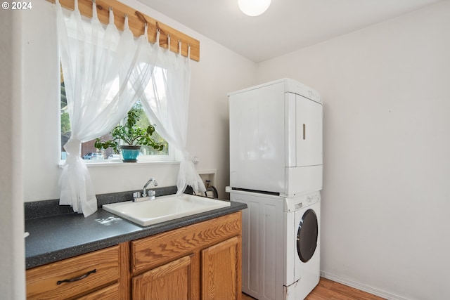 clothes washing area with light wood-type flooring, stacked washer and clothes dryer, cabinets, and sink