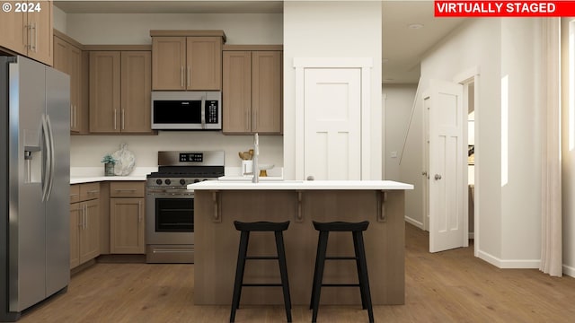 kitchen with stainless steel appliances, light wood-type flooring, light countertops, and a kitchen island with sink