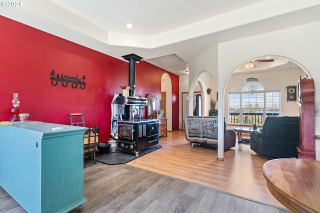 living room with hardwood / wood-style flooring, a tray ceiling, and a wood stove