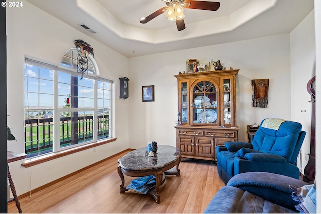 sitting room featuring a raised ceiling, ceiling fan, and light hardwood / wood-style flooring