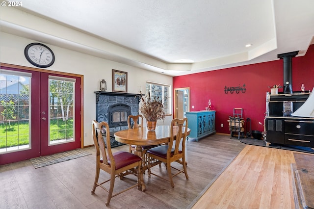 dining area with french doors, hardwood / wood-style flooring, a raised ceiling, and a wood stove