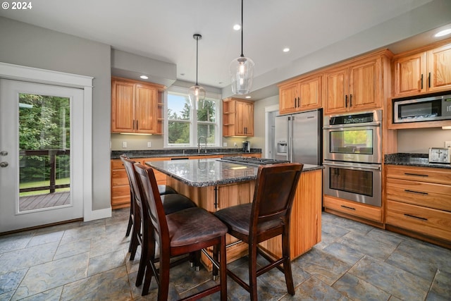 kitchen featuring dark stone countertops, a center island, decorative light fixtures, built in appliances, and a kitchen bar