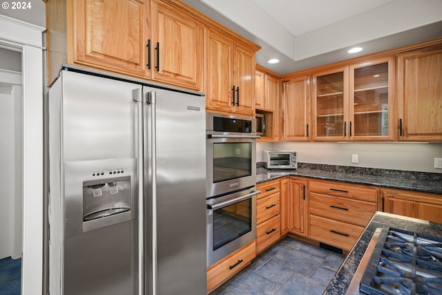 kitchen featuring dark stone countertops, a toaster, recessed lighting, stainless steel appliances, and glass insert cabinets