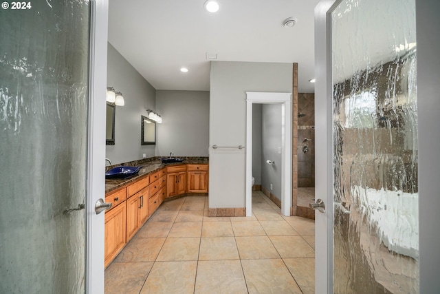 full bath with tile patterned flooring, double vanity, a tile shower, and a sink