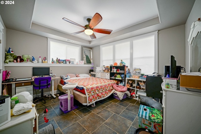 bedroom featuring a tray ceiling, stone finish flooring, visible vents, and ceiling fan