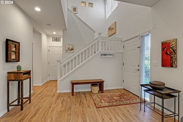 foyer with light wood-type flooring and a towering ceiling