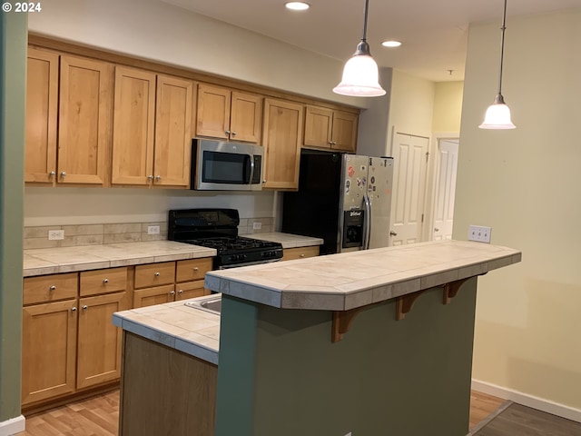 10733 NE Red Wing Way Unit 101, Hillsboro, OR 97006 - kitchen featuring stainless steel appliances, tile countertops, a breakfast bar, light wood-style flooring, and decorative light fixtures