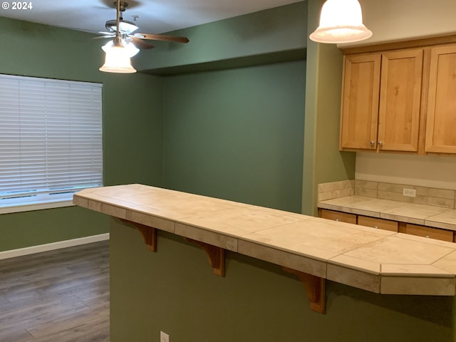 10733 NE Red Wing Way Unit 101, Hillsboro, OR 97006 - kitchen featuring tile countertops, a kitchen breakfast bar, a ceiling fan, dark wood-style floors, and baseboards