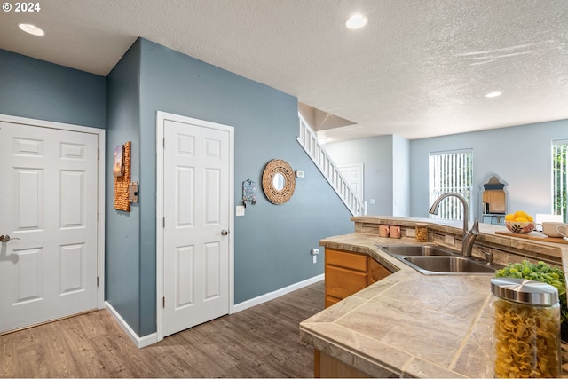 kitchen with a textured ceiling, dark wood-type flooring, tile countertops, and sink