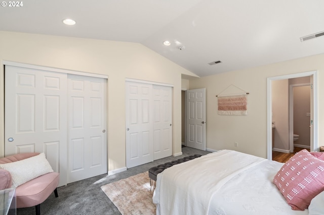 bedroom featuring dark carpet, lofted ceiling, ensuite bath, and two closets