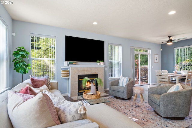 living room with ceiling fan, a textured ceiling, and a tiled fireplace