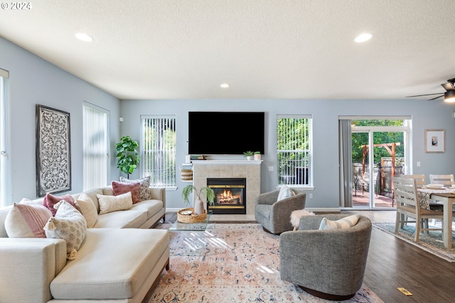 living room featuring a fireplace, ceiling fan, wood-type flooring, and a textured ceiling