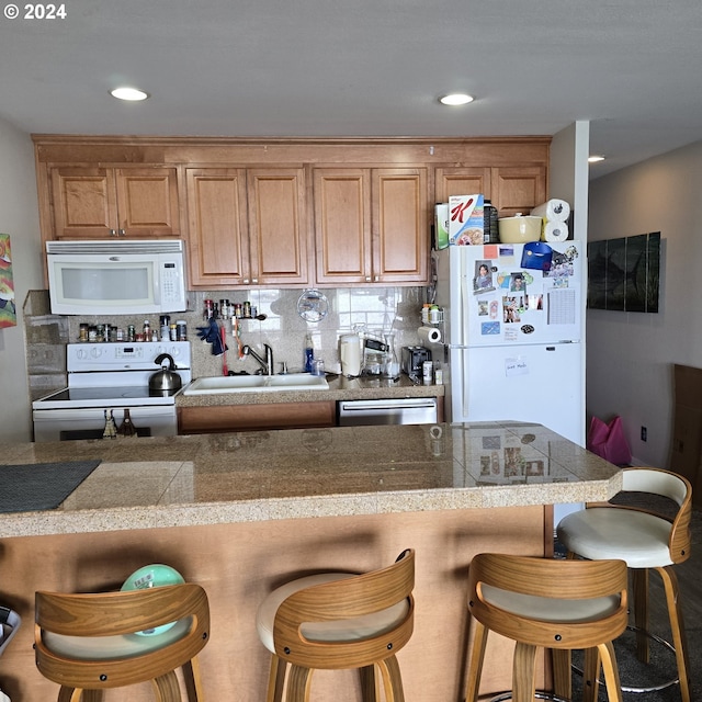 kitchen featuring white appliances, decorative backsplash, sink, and a breakfast bar area