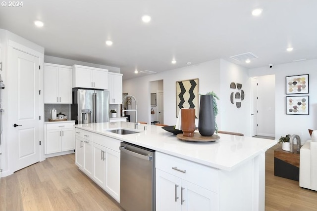 kitchen with appliances with stainless steel finishes, light wood-type flooring, a center island with sink, and white cabinetry