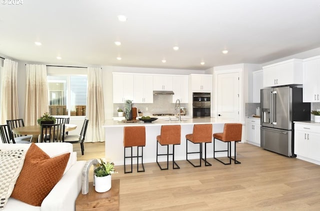 kitchen with white cabinets, appliances with stainless steel finishes, light wood-type flooring, and a kitchen breakfast bar