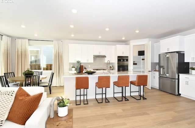 kitchen featuring a center island with sink, white cabinets, light wood-type flooring, and stainless steel appliances