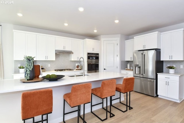 kitchen featuring stainless steel appliances, white cabinetry, a center island with sink, and sink